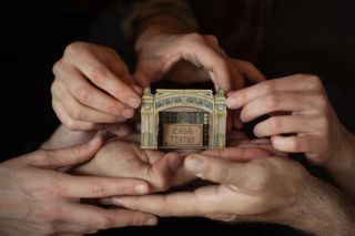 Image of hands with the house-Teatre between them